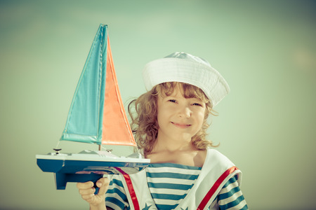 Happy kid playing with toy sailing boat against blue sky backgroundの写真素材