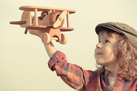 Happy kid playing with toy airplane against summer sky backgroundの写真素材