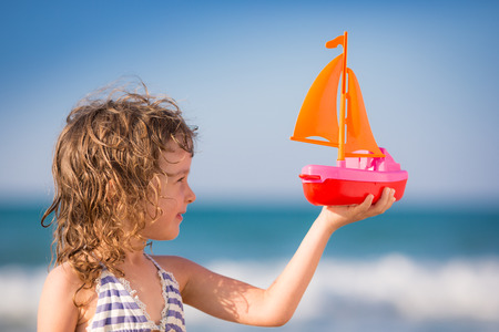 Happy kid playing with toy sailing boat against blue sky backgroundの写真素材