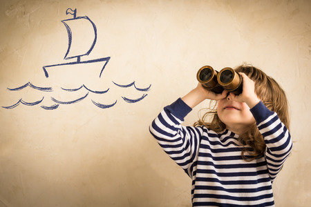 Happy sailor kid playing indoors. Smiling child look at drawing ship. Travel and adventure concept. Summer vacationの写真素材