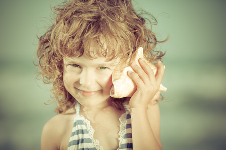 Beautiful child at the beach. Smiling kid listen sea. Summer vacation concept. Toned imageの写真素材