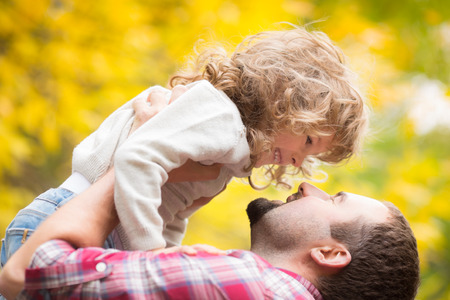 Happy family having fun outdoors in autumn park against yellow blurred leaves backgroundの写真素材