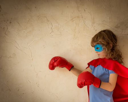 Superhero child dressed in red cape, boxing gloves and blue mask against grunge wall backgroundの写真素材