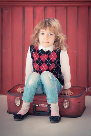 Sad child sitting on red suitcase indoors. Travel and freedom conceptの写真素材