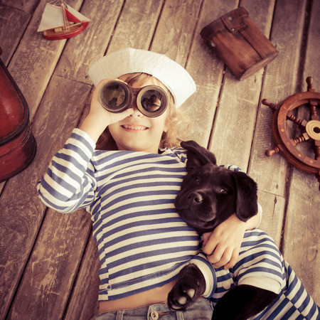 Happy kid dressed in sailor. Child playing with dog at home. Travel and adventure conceptの写真素材