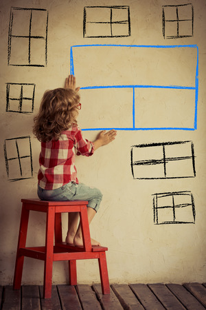 Sad child sitting against old wall with drawn window. Freedom and imagination conceptの写真素材