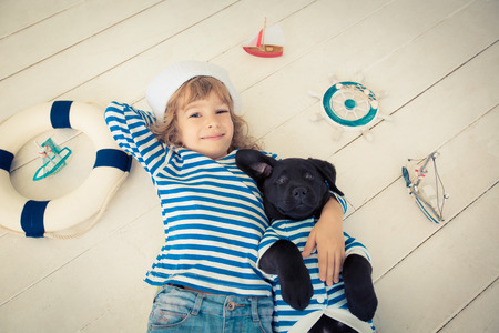 Happy kid dressed in sailor. Child playing with dog at home. Travel and adventure conceptの写真素材
