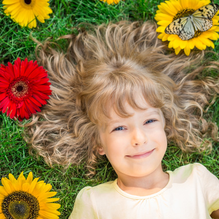 Beautiful child with butterfly in spring park. Happy kid lying on green grass outdoorsの写真素材