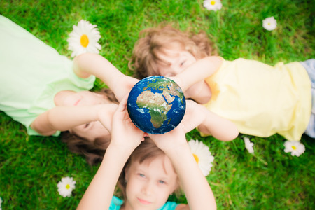 Children holding 3D planet in hands against green spring background. Earth day holiday concept. Elements of this image furnished by NASAの写真素材