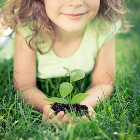 Child holding young green plant in hands. Kid lying on grass in spring park. Earth day conceptの写真素材