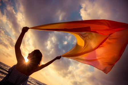 Silhouette of young woman jumping with silk fabric at the beach. Summer vacation conceptの写真素材
