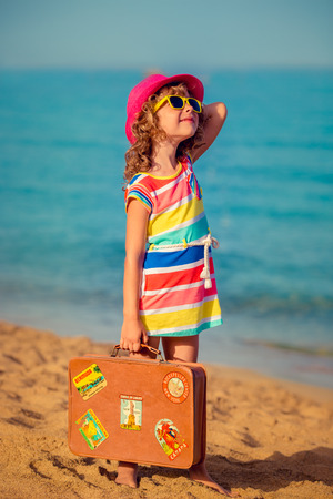 Happy child with vintage suitcase on the beach. Summer vacation and travel conceptの写真素材