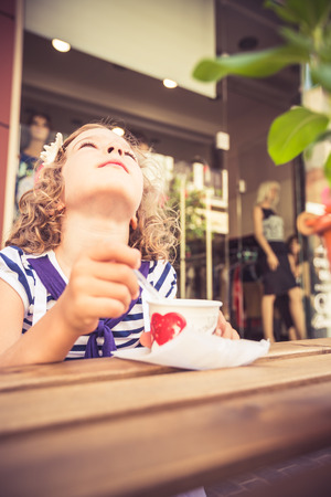 Happy child eating ice-cream in summer cafe outdoorsの写真素材