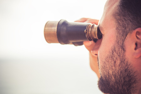 Sailor man looking through the binoculars against blue sky backgroundの写真素材