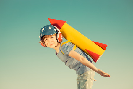 Happy child playing with toy rocket against summer sky background. Retro tonedの写真素材