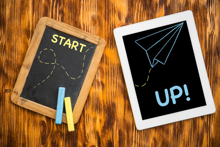 Tablet PC and blackboard on wooden desk in class. Education concept. Top viewの写真素材