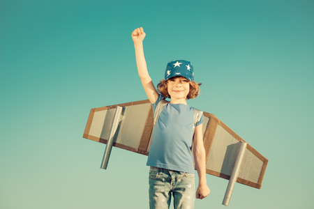 Happy child playing with toy wings against summer sky background. Retro tonedの写真素材