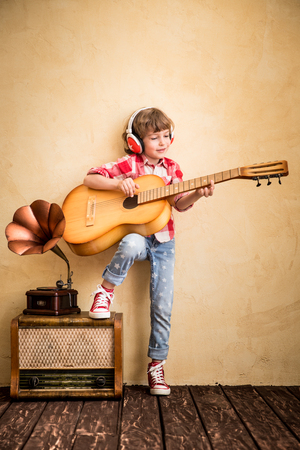 Kid listen music at home. Hipster child with retro vintage acoustic guitarの写真素材