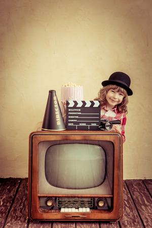 Child playing at home. Funny girl holding clapper board. Retro TV. Cinema conceptの写真素材