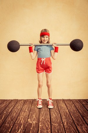 Funny strong child with barbell. Girl power and feminism concept. Sport fitness success winner kidの写真素材