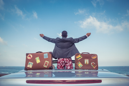 Successful young businessman on a beach. Man standing in the cabriolet classic car. Summer vacations and travel conceptの写真素材