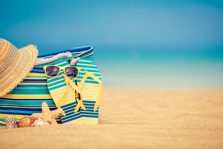 Flip-flops and bag on sandy beach against blue sea and sky background. Summer vacation conceptの写真素材