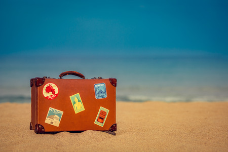 Vintage suitcase on sandy beach against blue sea and sky background. Summer vacation and travel conceptの写真素材