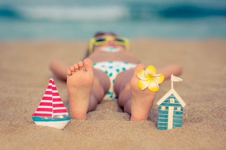 Child lying on sandy beach near blue sea. Summer vacation and healthy lifestyle conceptの写真素材
