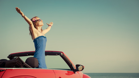 Young woman relaxing on the beach. Girl having fun in red cabriolet against toned sky background. Summer vacation and travel conceptの写真素材