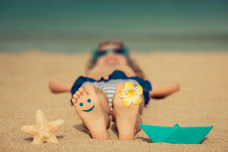 Child lying on sandy beach near blue sea. Summer vacation and healthy lifestyle conceptの写真素材