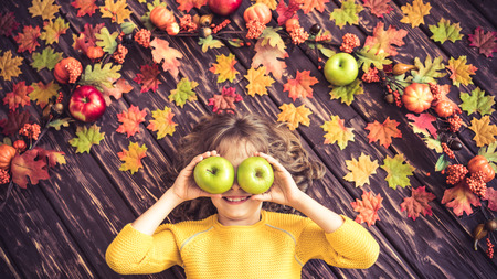 Happy child lying on autumn leaves. Top view portrait of funny kid at home. Thanksgiving holiday conceptの写真素材