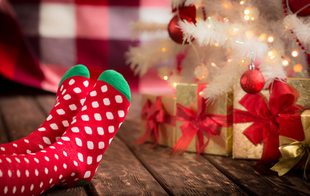 Children feet in Christmas socks near Xmas tree. Girl relaxing at home. Winter holiday Xmas and New Year conceptの写真素材