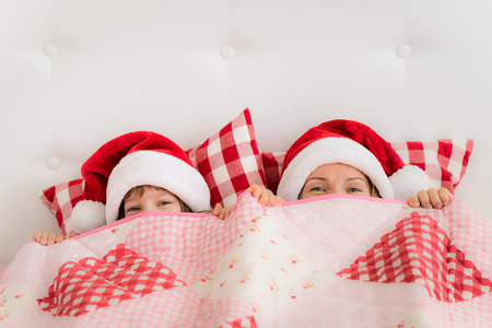 Family in Christmas Santa hats lying on bed. Mother and daughter having fun in bedroom. People relaxing at home. Winter holiday Xmas and New Year conceptの写真素材