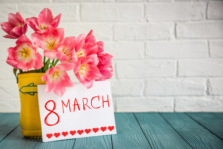 Bouquet of tulips in rain boots on wood table. Woman's day. 8 March. Spring holiday concept Bouquet of tulips in rain boots on wood table. Woman's day. 8 March. Spring holiday concept