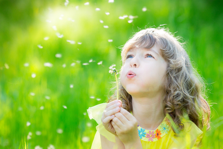 Happy child blowing dandelion flower outdoors. Girl having fun in spring park. Blurred green background. Dream and imagination conceptの写真素材