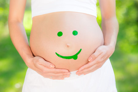 Beautiful belly of young pregnant woman against green spring background