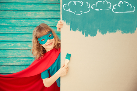 Superhero child painting the wall with blue color. Kid having fun at home. Spring renovation conceptの写真素材