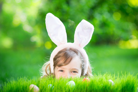 Easter bunny. Child having fun outdoor. Kid playing with eggs on green grass. Spring holidays...