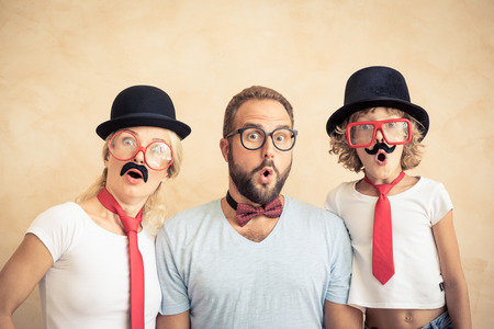 Funny man, woman and kid with fake mustache. Happy family playing in home