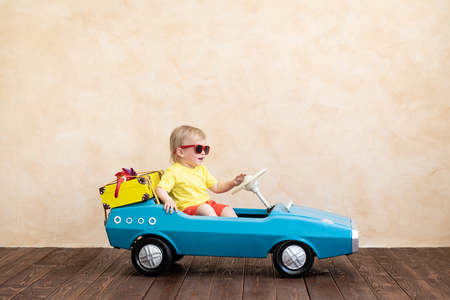 Happy child riding toy vintage car. Funny kid playing at home. Summer vacation and travel conceptの写真素材