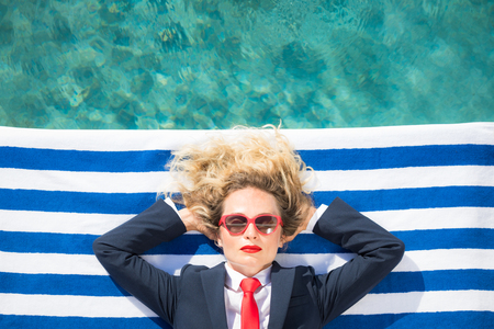 Successful young businesswoman on the beach. Woman lying on striped towel near swimming pool. Summer vacations and freedom travel conceptの写真素材