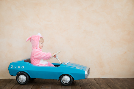 Funny kid wearing Easter bunny. Child riding toy car at home. Spring holidays conceptの写真素材