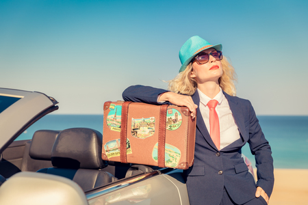 Successful young businesswoman on the beach. Woman standing near the cabriolet classic car. Summer vacations and freedom travel conceptの写真素材