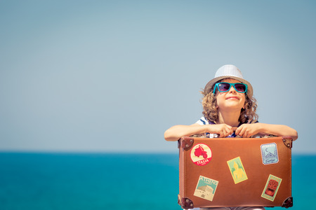 Happy child with suitcase on the beach. Kid enjoys a summer vacation at the sea. Travel and holiday conceptの写真素材