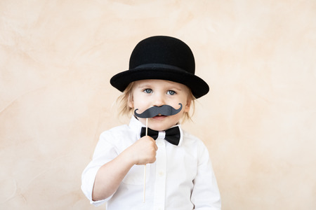 Funny kid with fake paper moustache. Happy child playing in home. Father's day conceptの写真素材