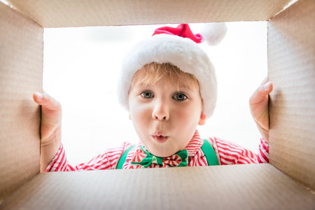 Happy child looking into the box. Funny surprised baby boy unpack Christmas gift box. Xmas holiday concept. Low angle view.の写真素材