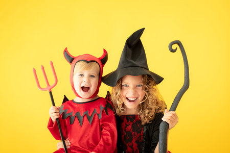 Happy children dressed Halloween costume. Portrait of funny kids against yellow background.