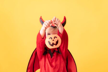 Funny child dressed devil costume against yellow background. Happy Halloween holidays conceptの写真素材