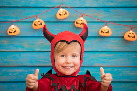 Happy child dressed Halloween costume. Portrait of funny kid against wooden background.