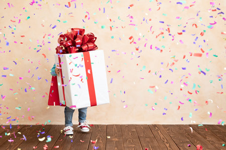 Happy child dressed superhero holding Christmas gift box. Funny kid wearing super hero costume with...